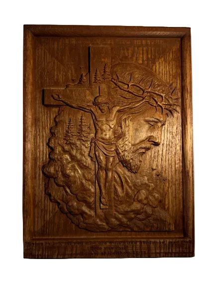 A carved wooden wall plaque featuring a relief scene of Jesus on the cross with a crown of thorns, set against a plain light gray wall